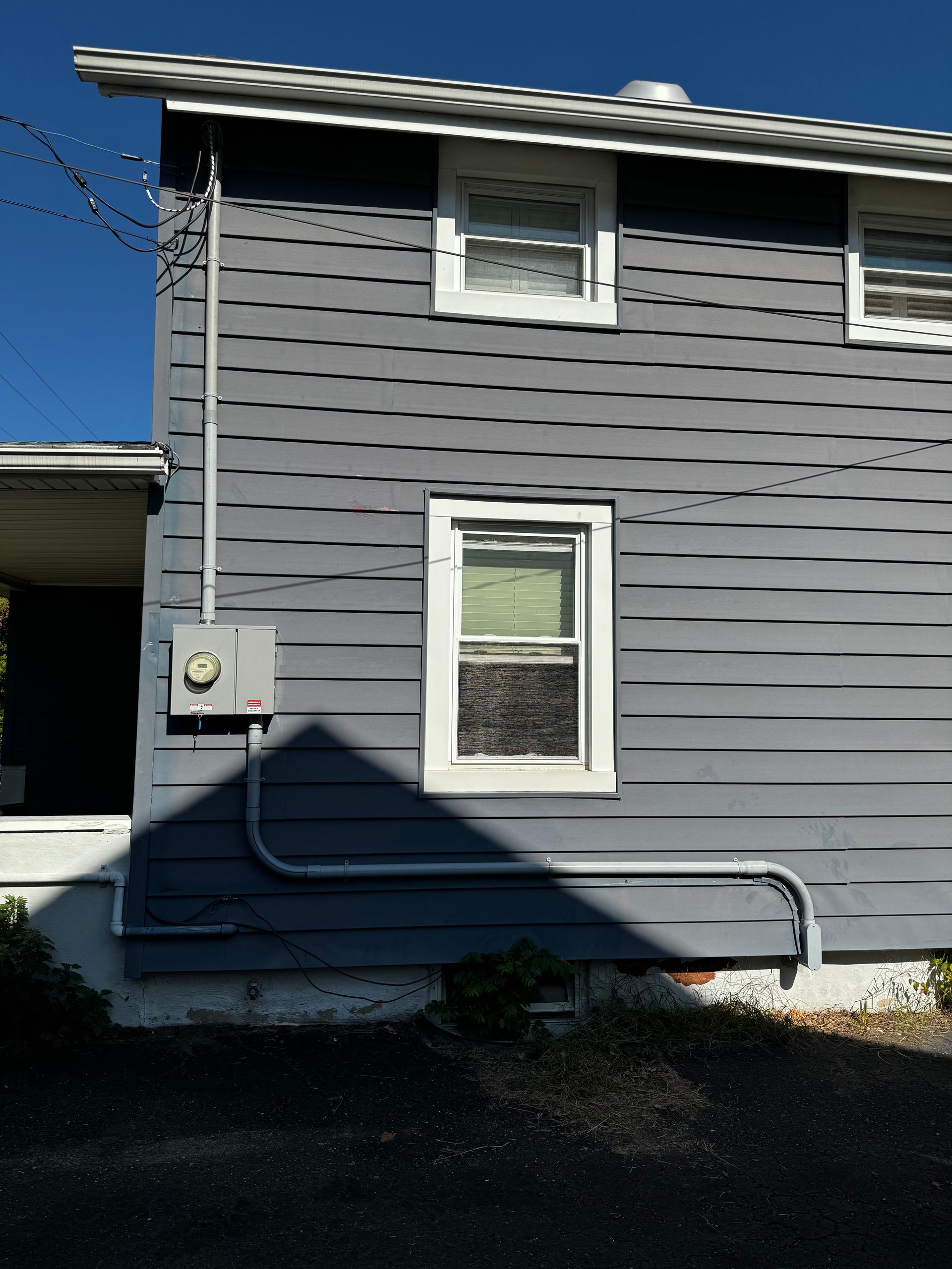 Side of a gray house with white-framed windows, electrical box, and conduit.