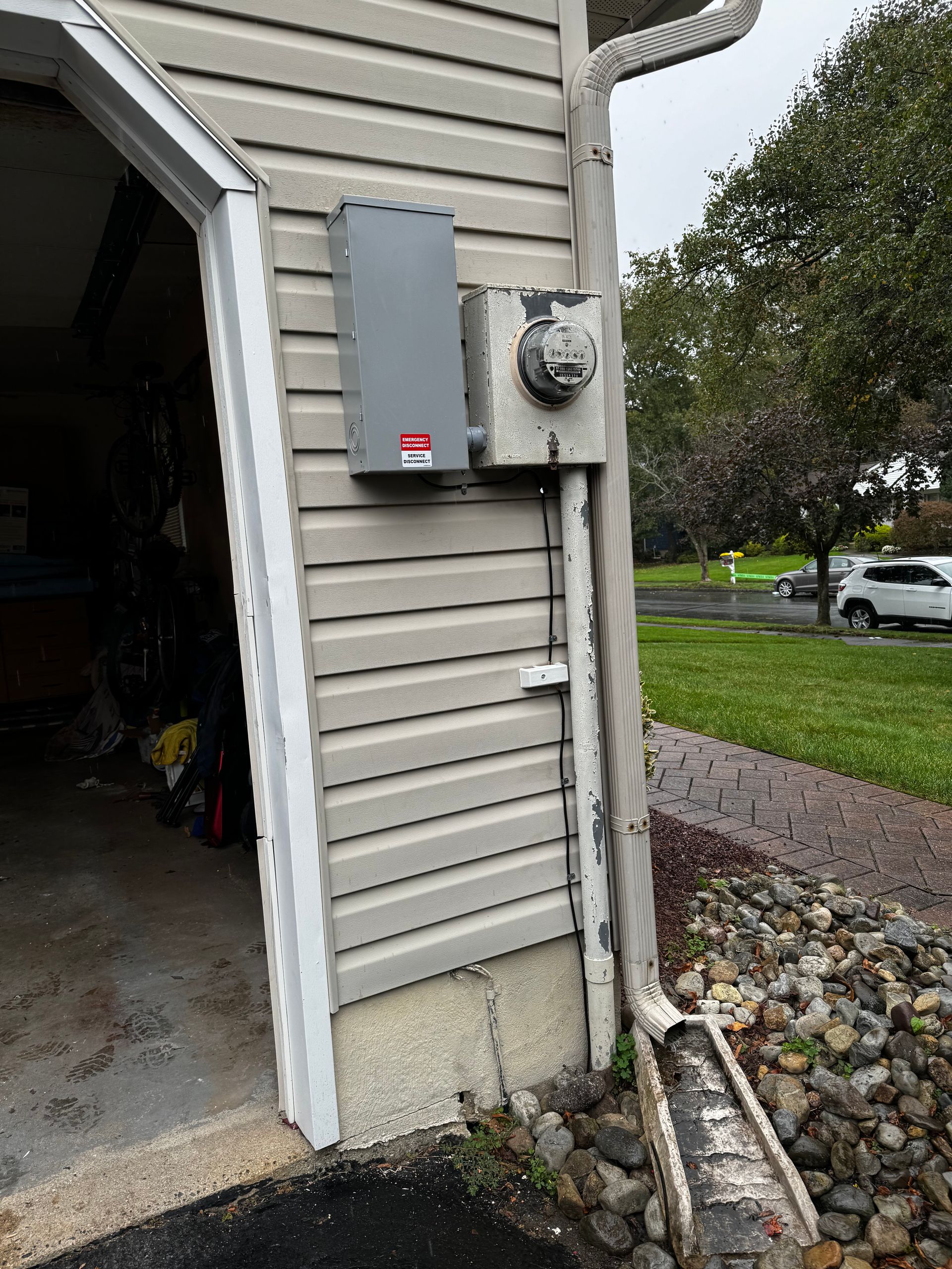 Gray electrical panel and meter on a beige house exterior next to a garage door.