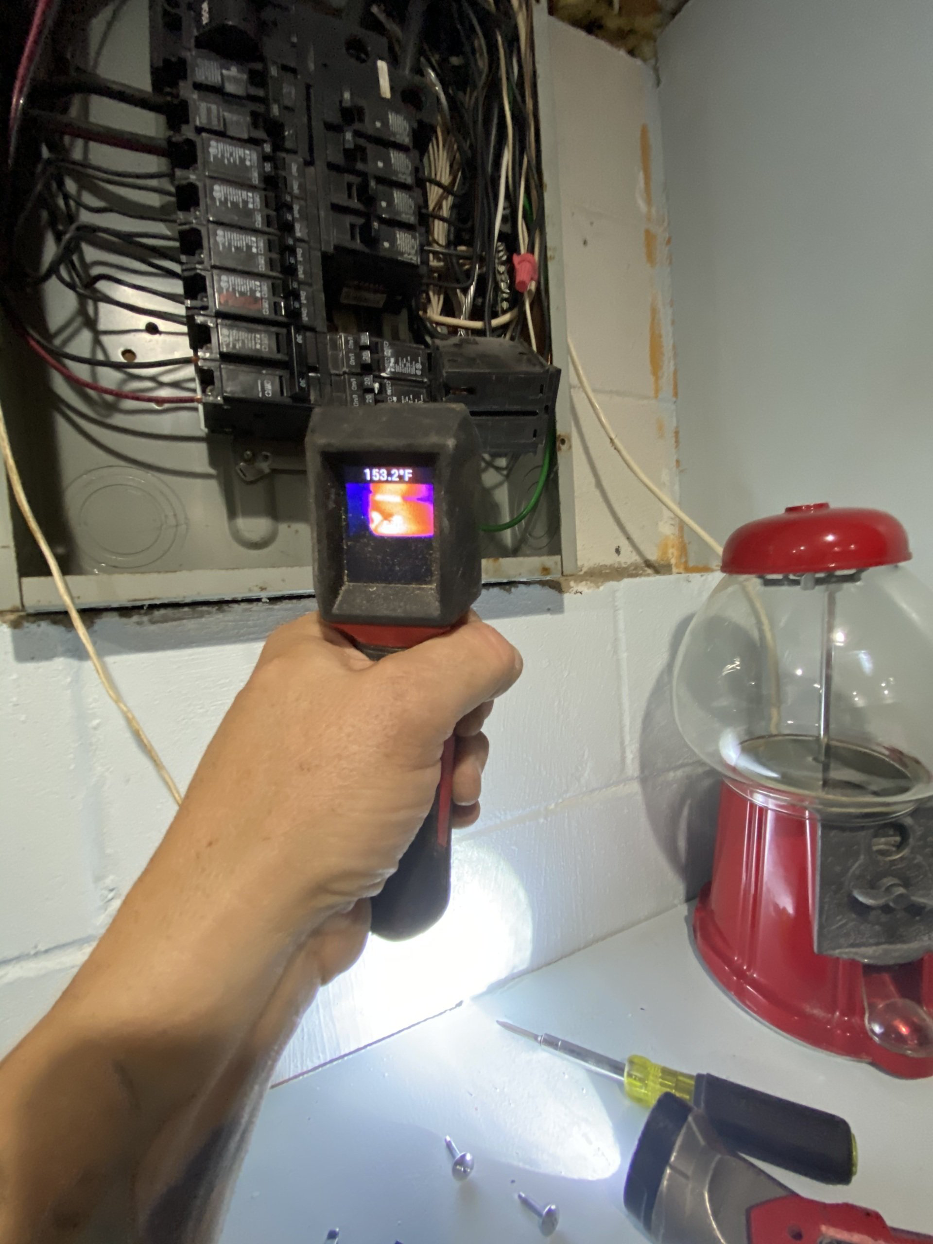 Hand holding thermal camera pointed at electrical panel, potentially detecting heat.