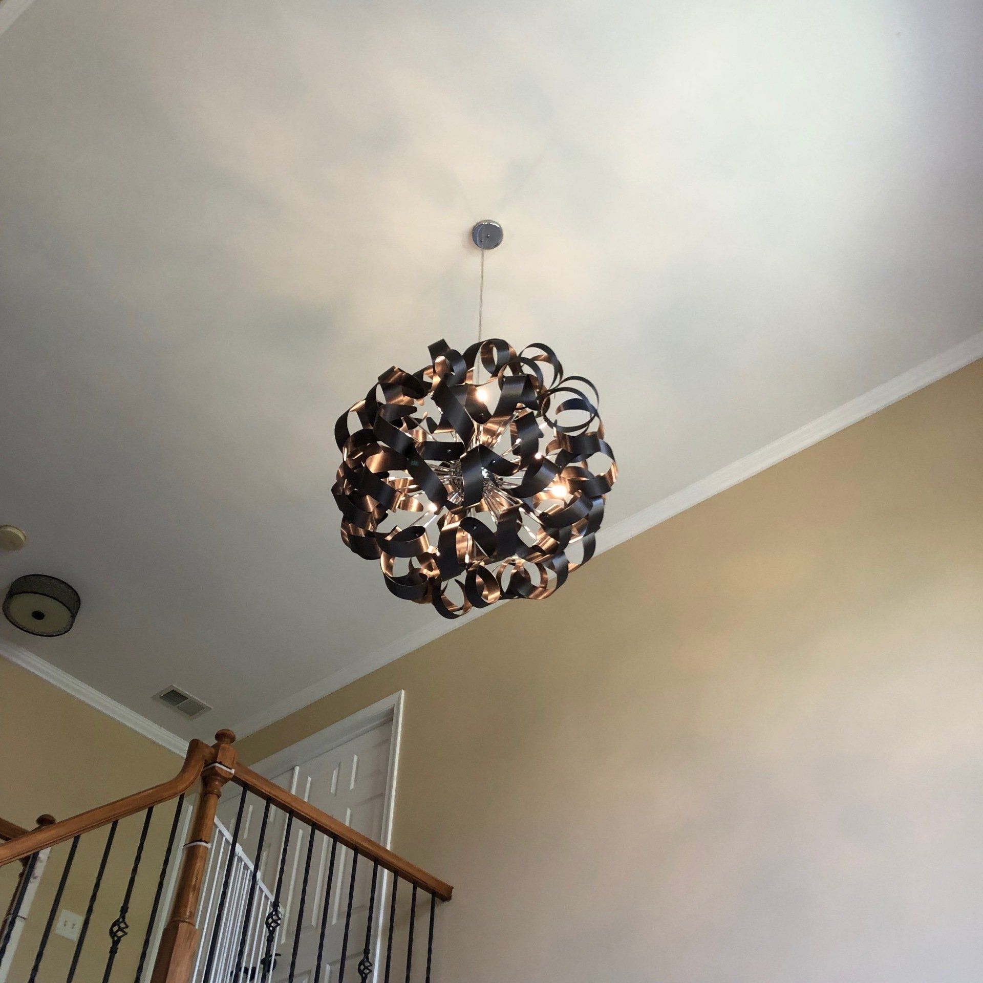 Dark orb-shaped chandelier hanging from a white ceiling over a staircase.