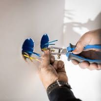 Electrician in yellow hard hat working on wall wiring.