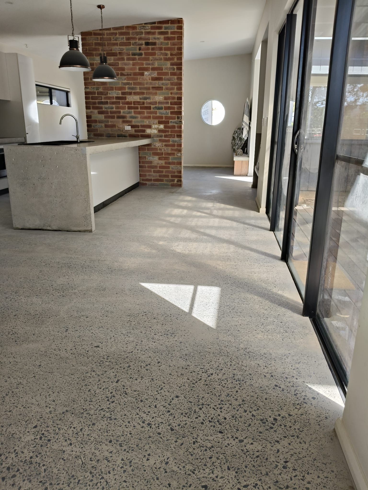 Modern kitchen with Full Exposure concrete floors, a brick accent wall, a central island, and floor-to-ceiling glass doors.