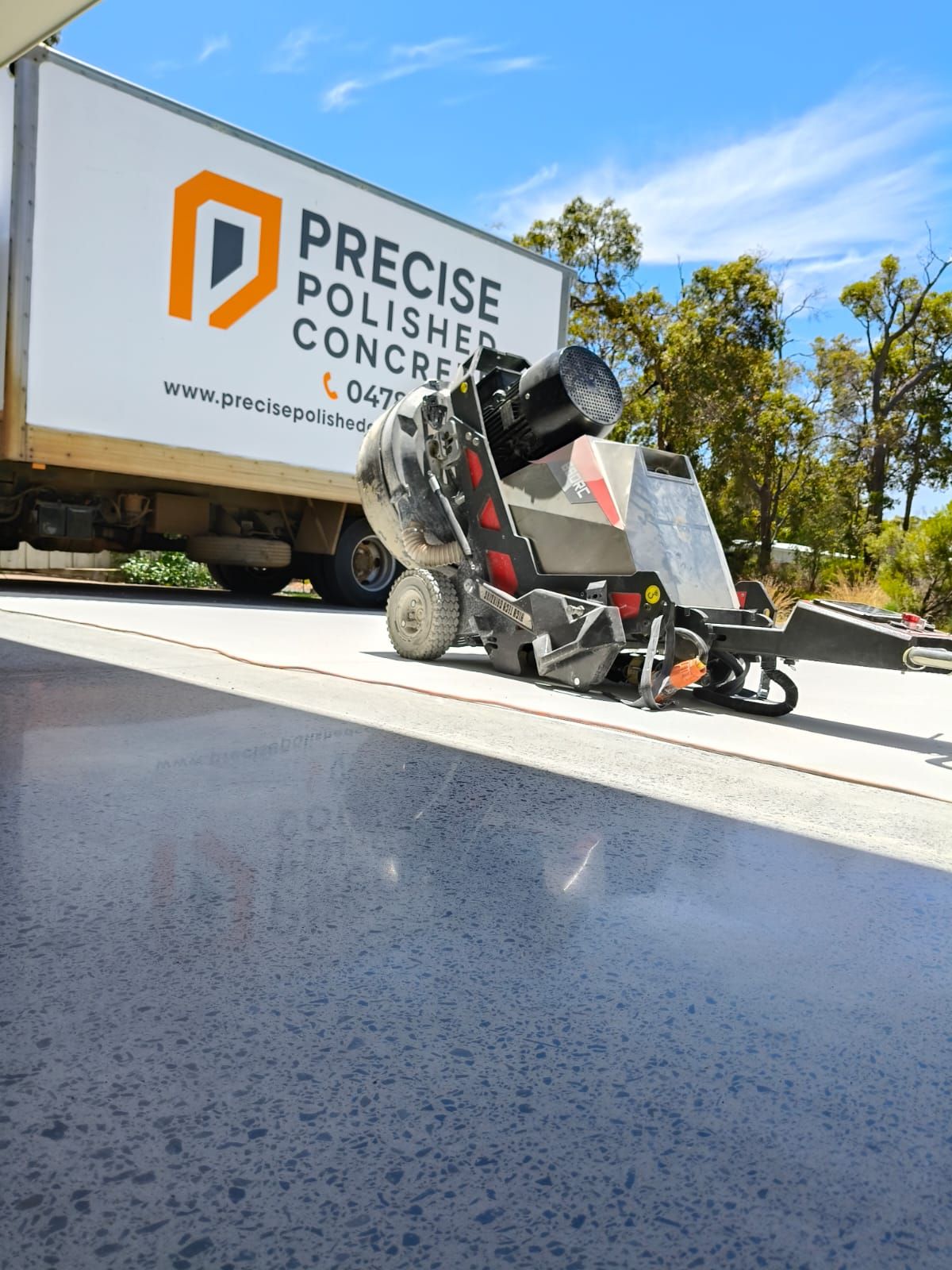 Concrete polishing machine working on a concrete surface, with a truck from