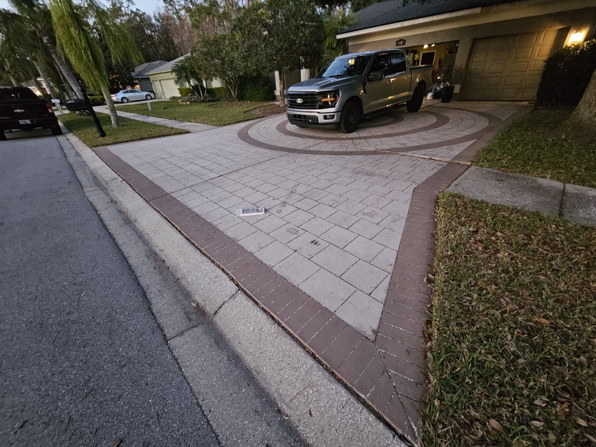 Paver driveway with a truck parked in the circular turn-around. A curb and street are to the left.