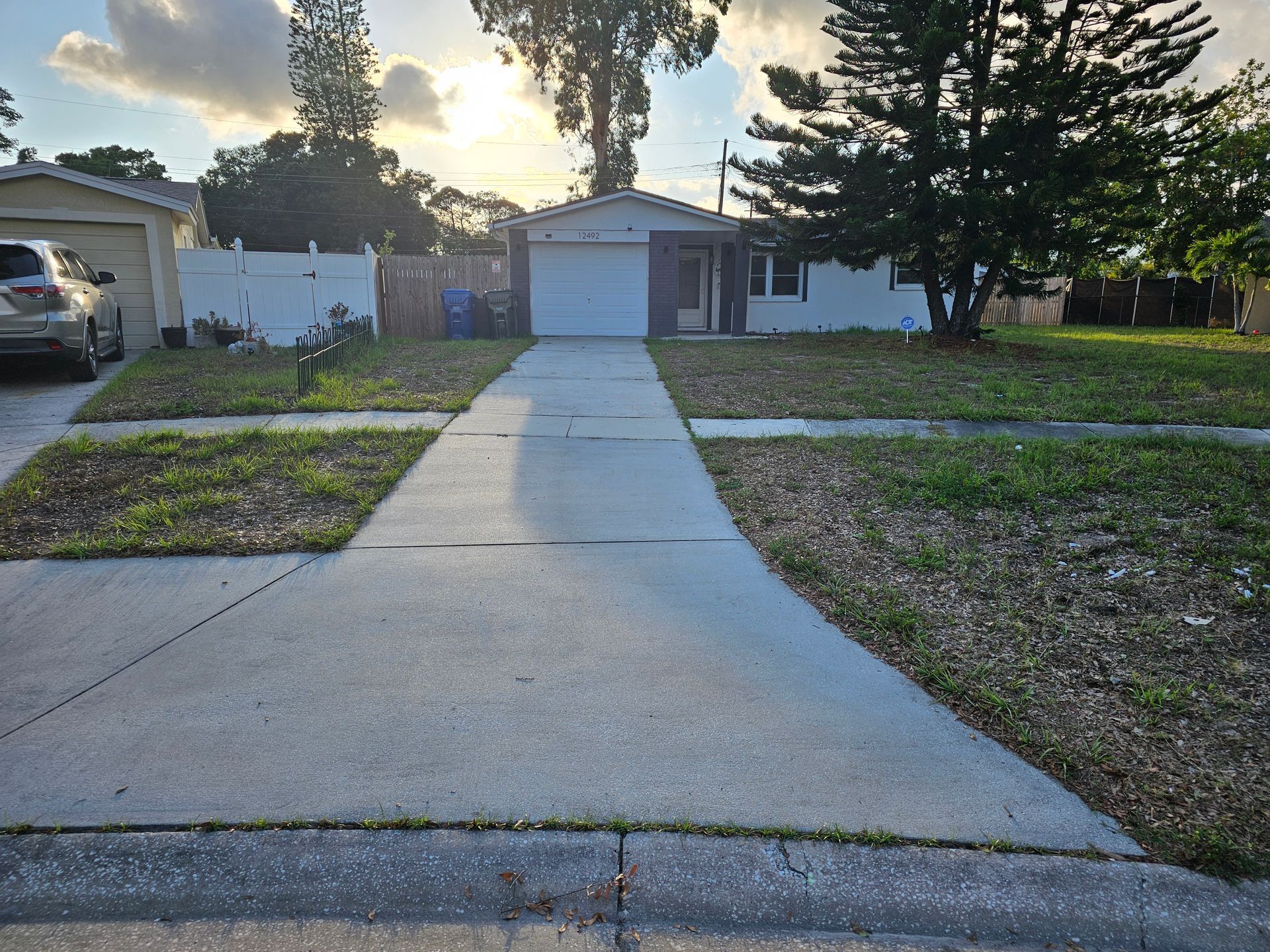 Suburban house with driveway, garage, and patchy lawn under a bright sky.
