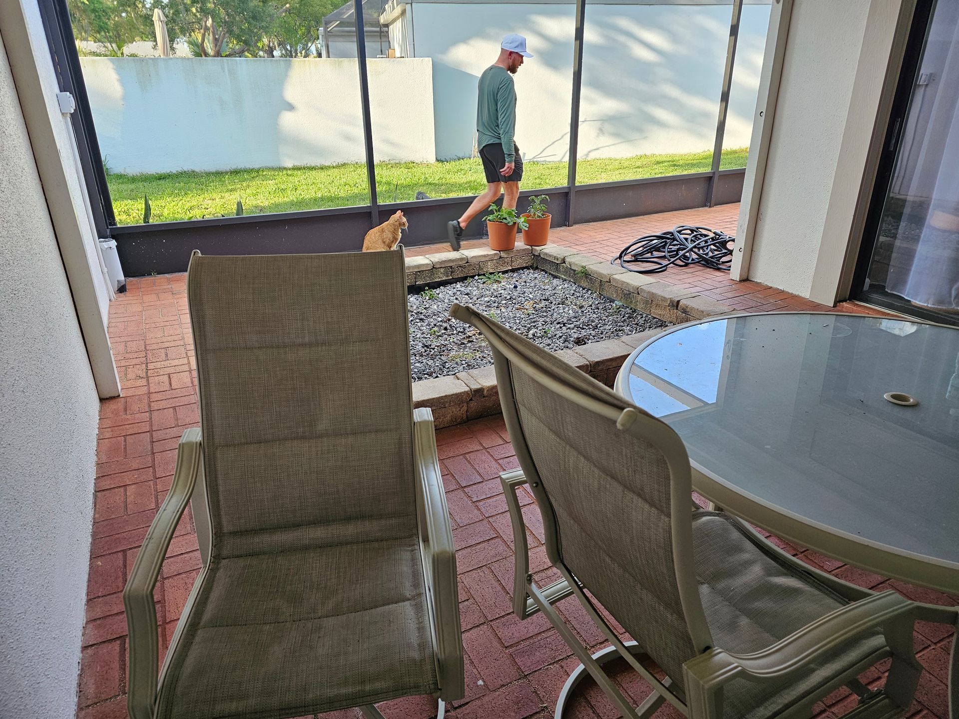Patio scene: man walking, cat near fire pit, two chairs, table.