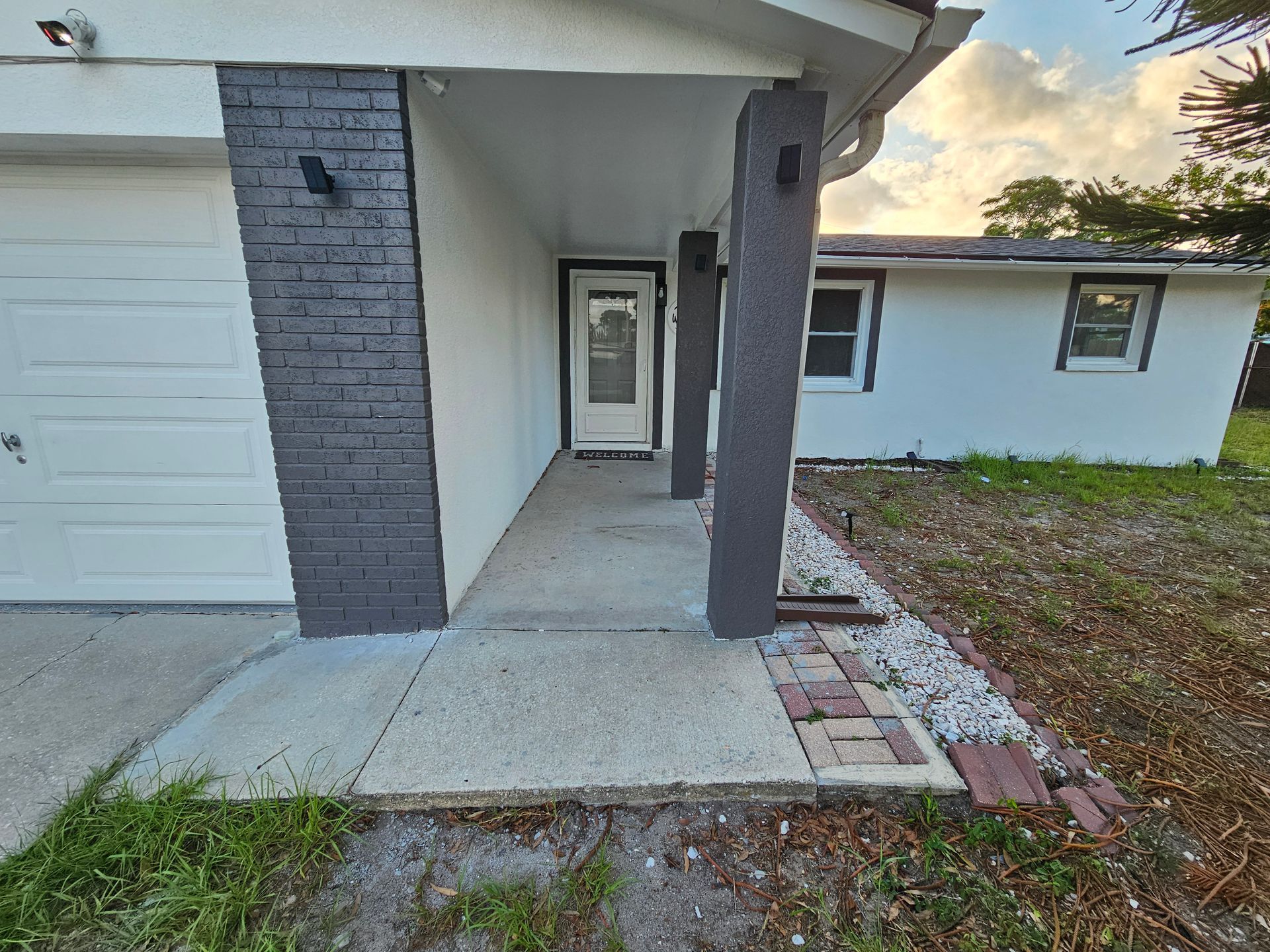 Exterior of a white house with a covered entrance, gray columns, brick accents and walkway.