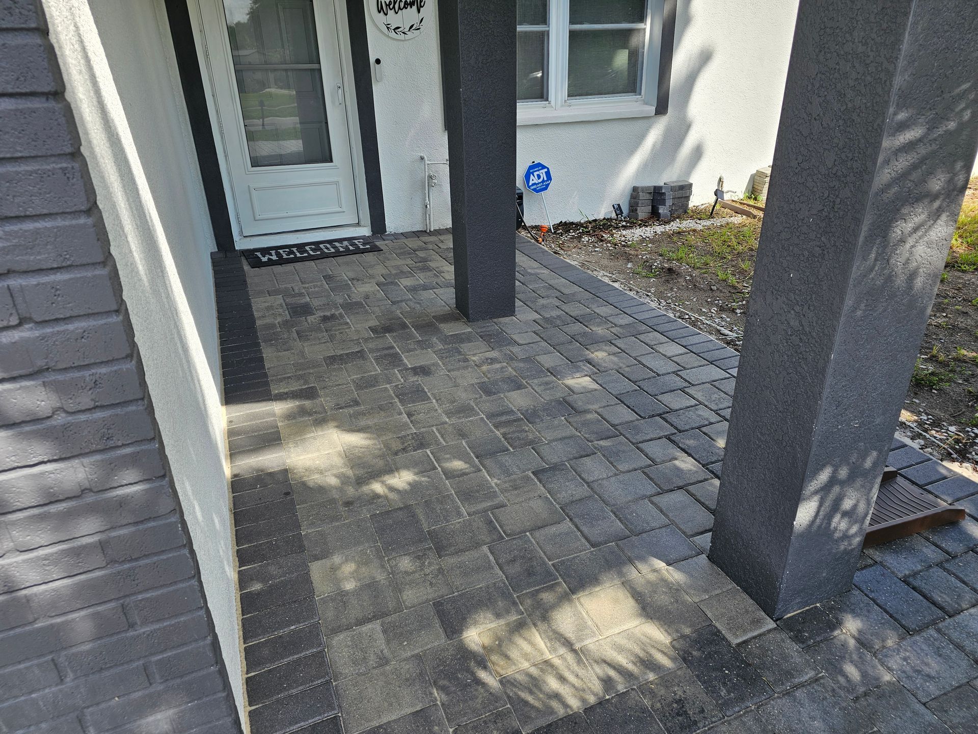 Porch with gray brick pavers, pillars, and a front door with 