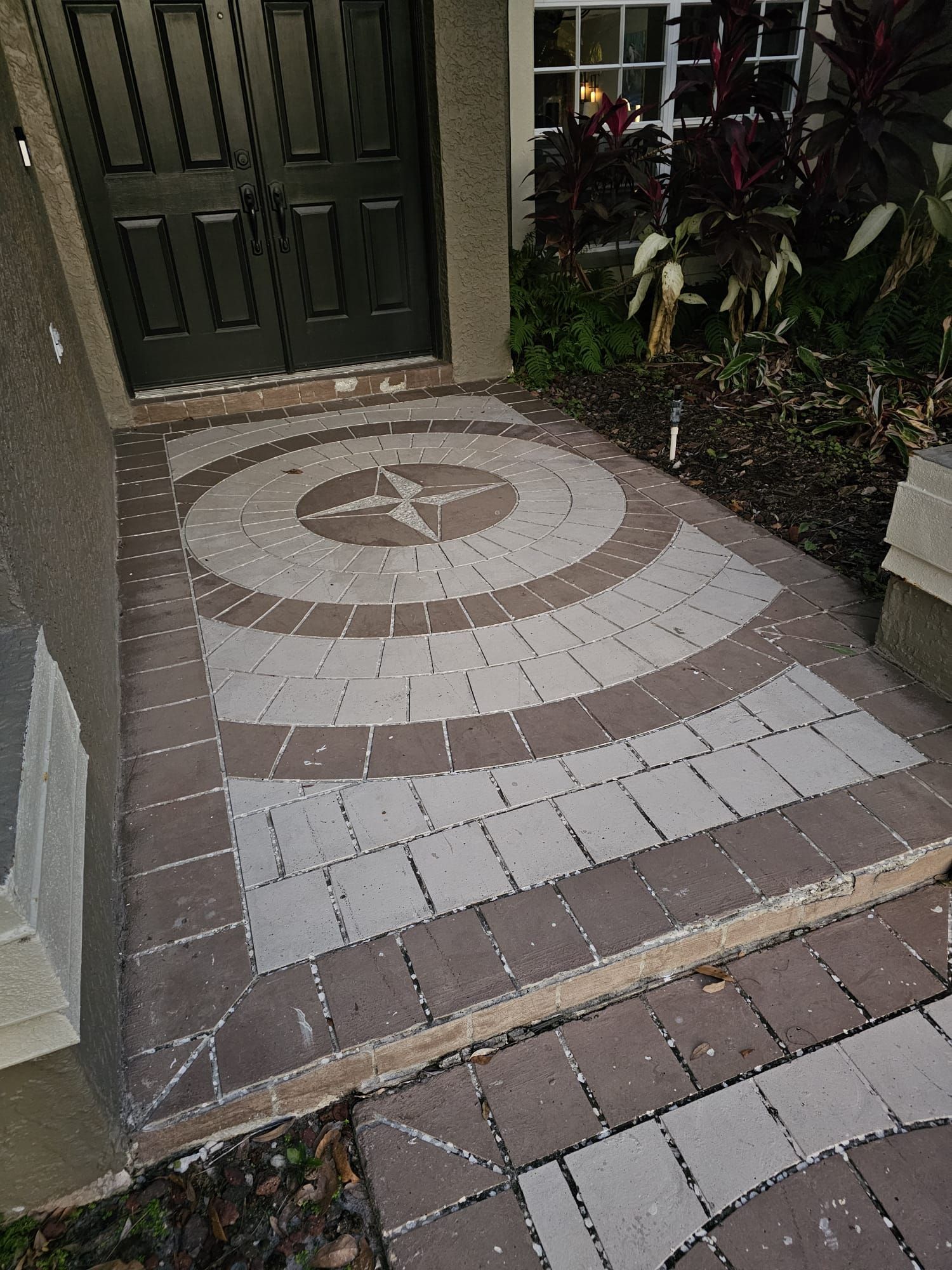 Brick walkway with compass design leading to a dark front door.