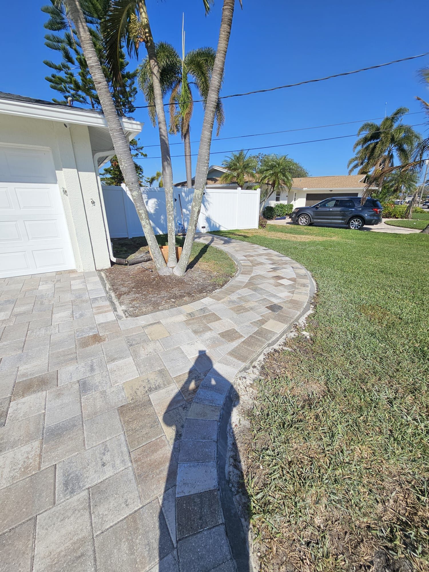 A paved walkway curves through a grassy yard toward a white house under a blue sky.