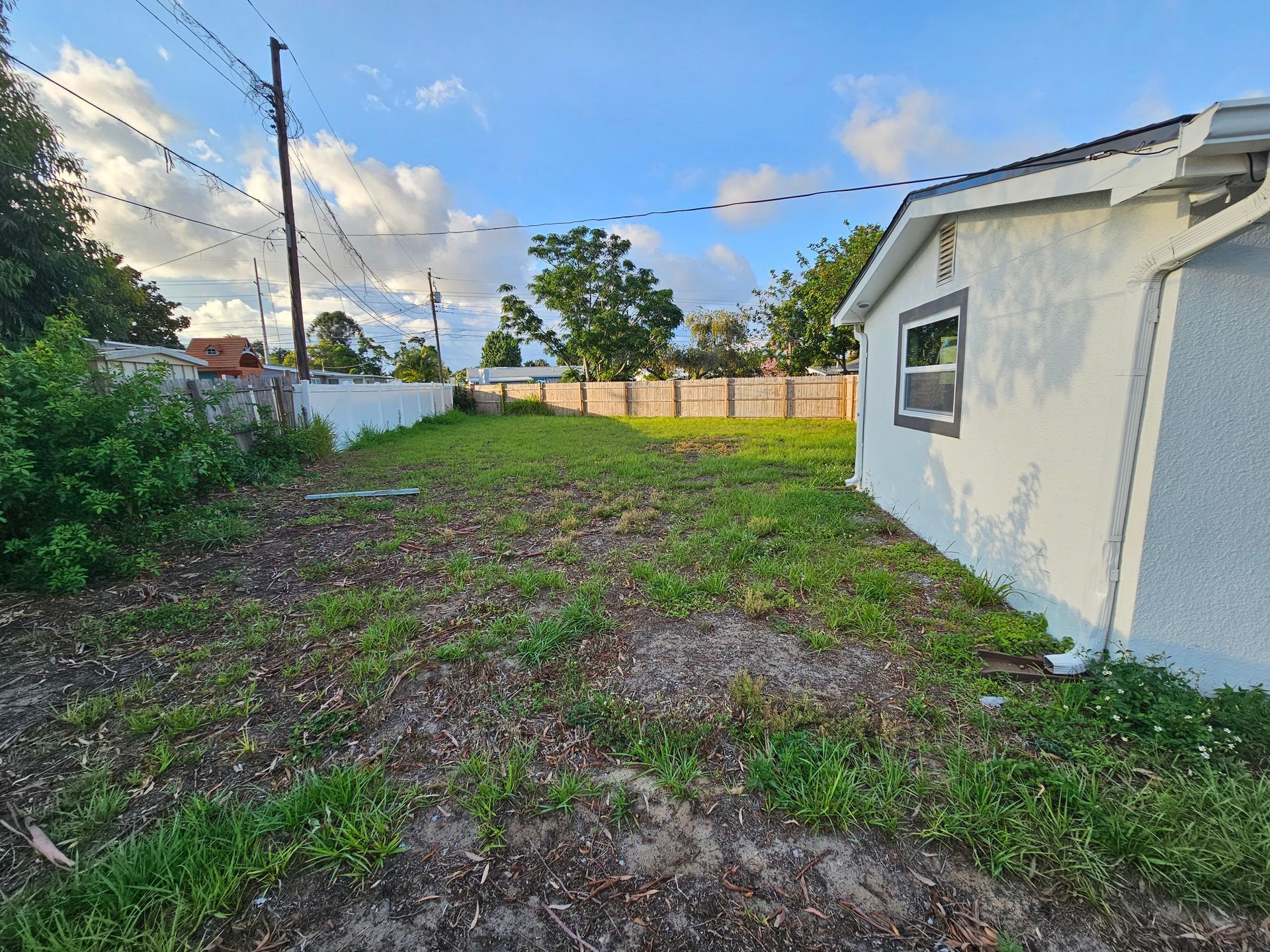 Grassy backyard with a small white building on the right and a fence along the back under a cloudy sky.