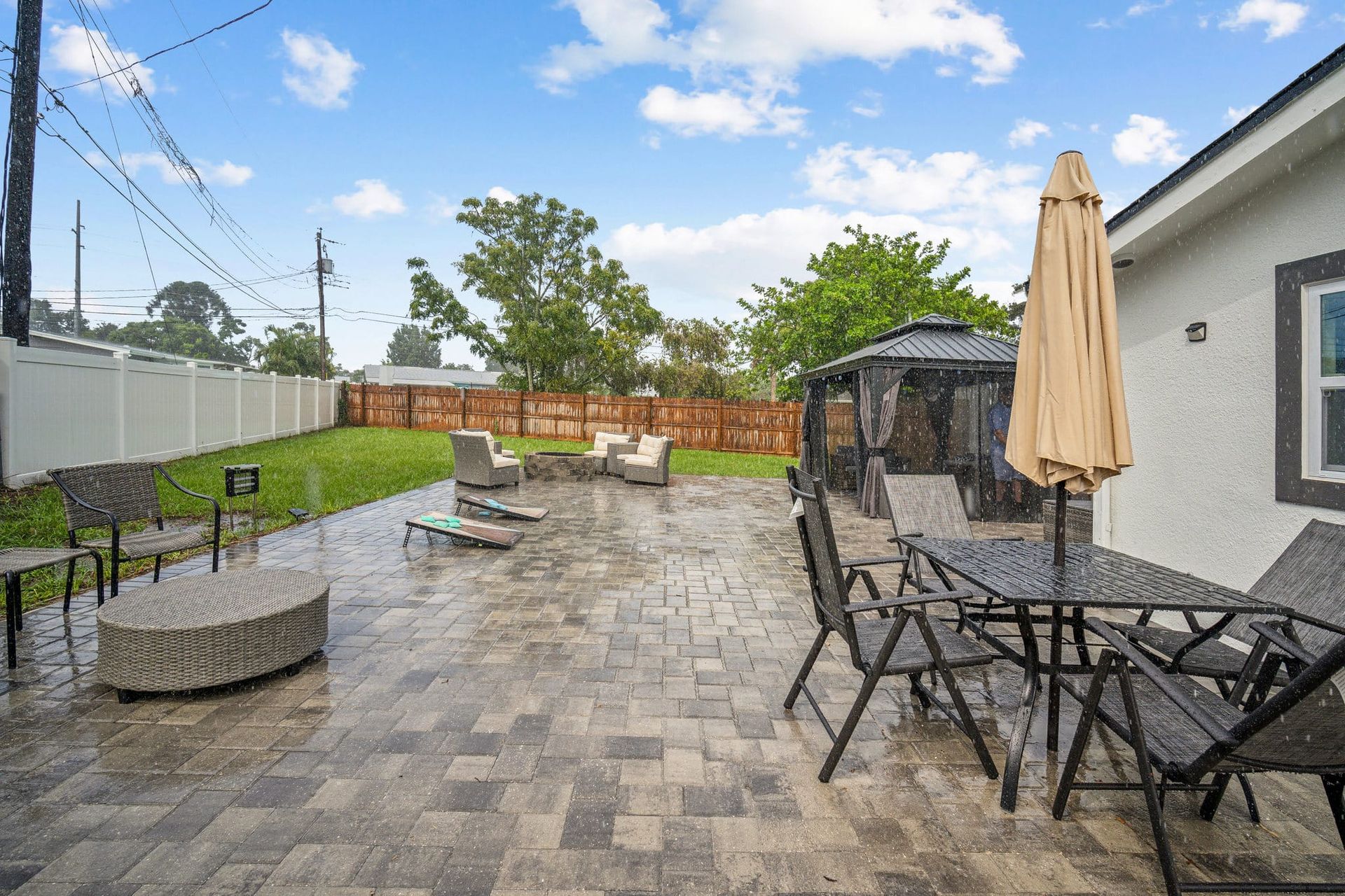 Patio with stone pavers, furniture, gazebo, and fire pit under a cloudy sky.