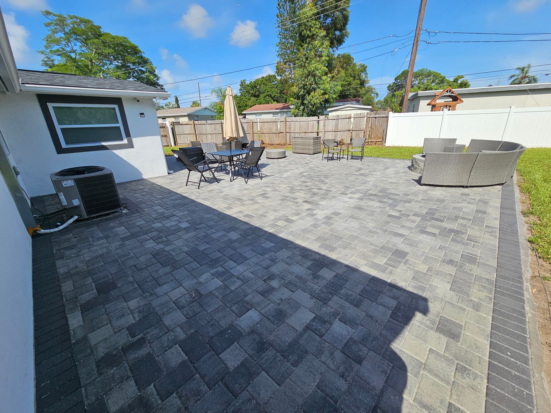 Patio with gray pavers, outdoor furniture, and surrounding white fence, sunny day.