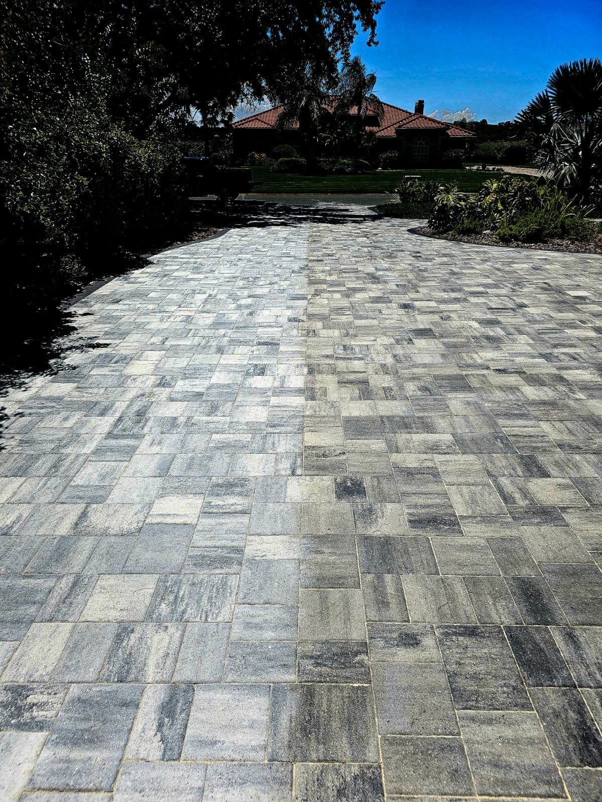 Brick driveway leading to a house with a red roof. Blue sky and trees are visible.