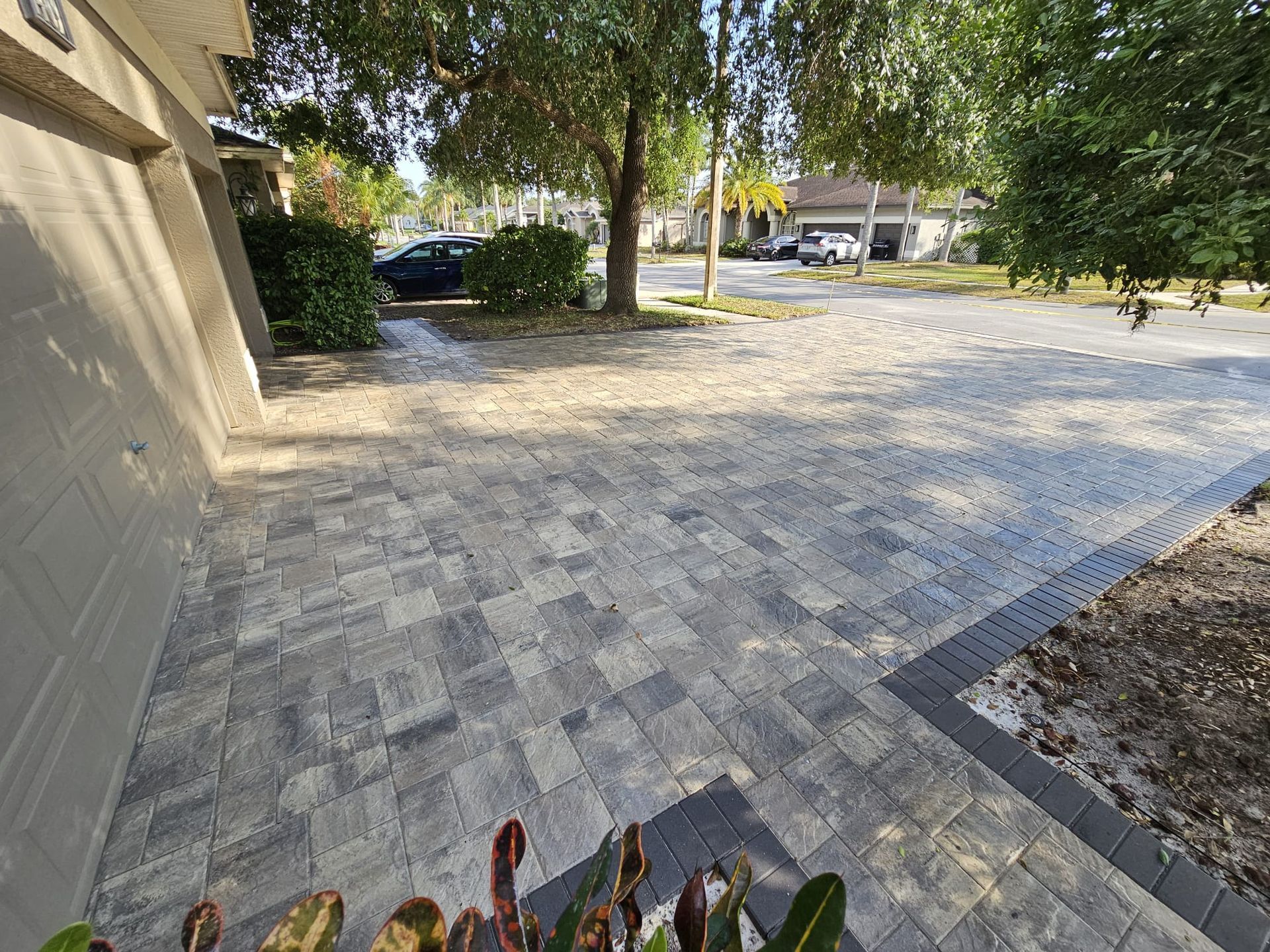Paver driveway in front of a house with a tree and street in the background.
