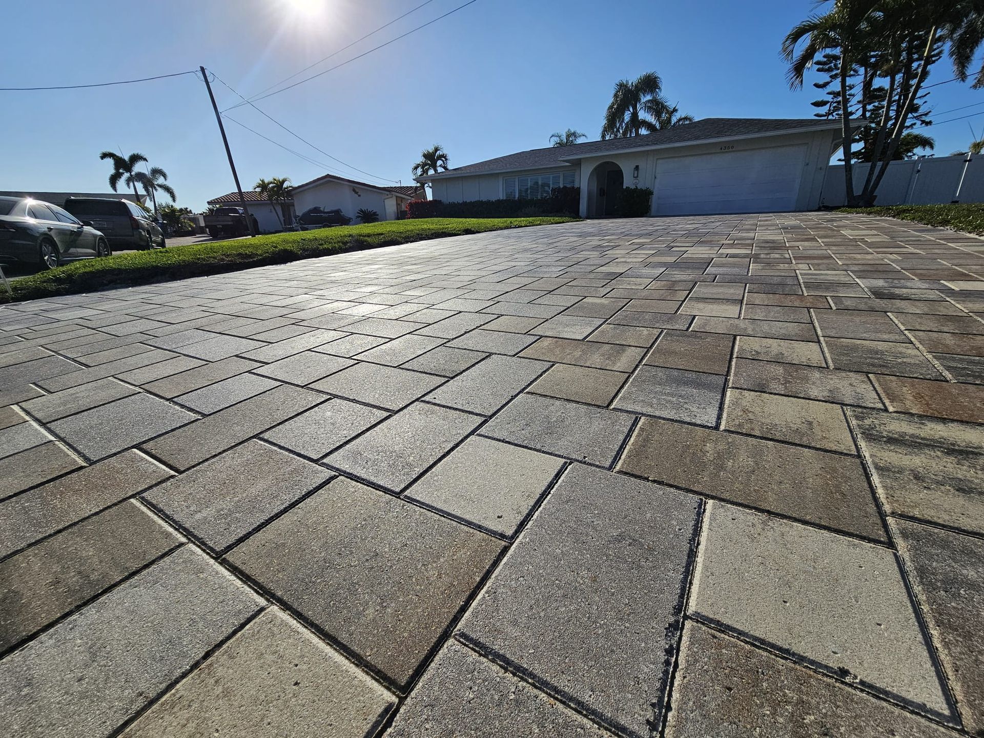Brick paver driveway leading to a house under a sunny blue sky.