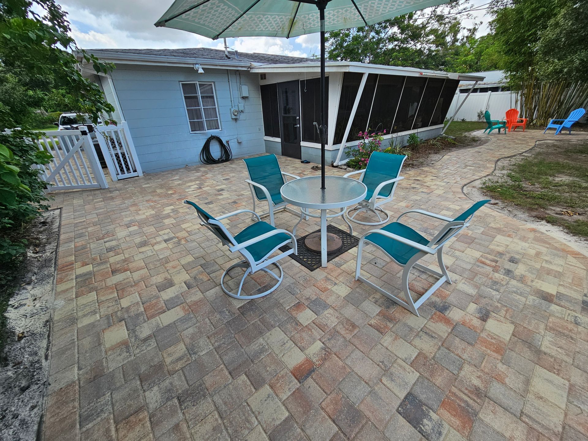 Patio with a table, chairs, and umbrella in front of a light blue house with a screened porch.