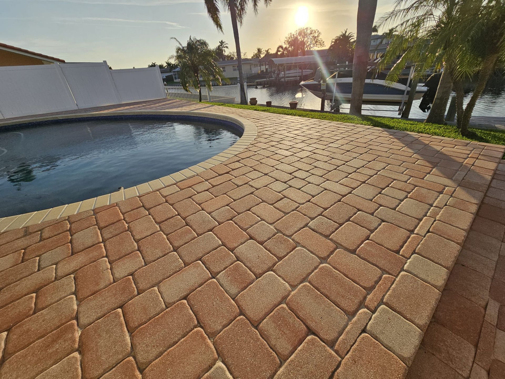 Brick patio surrounding a pool; canal and sunset in the background.