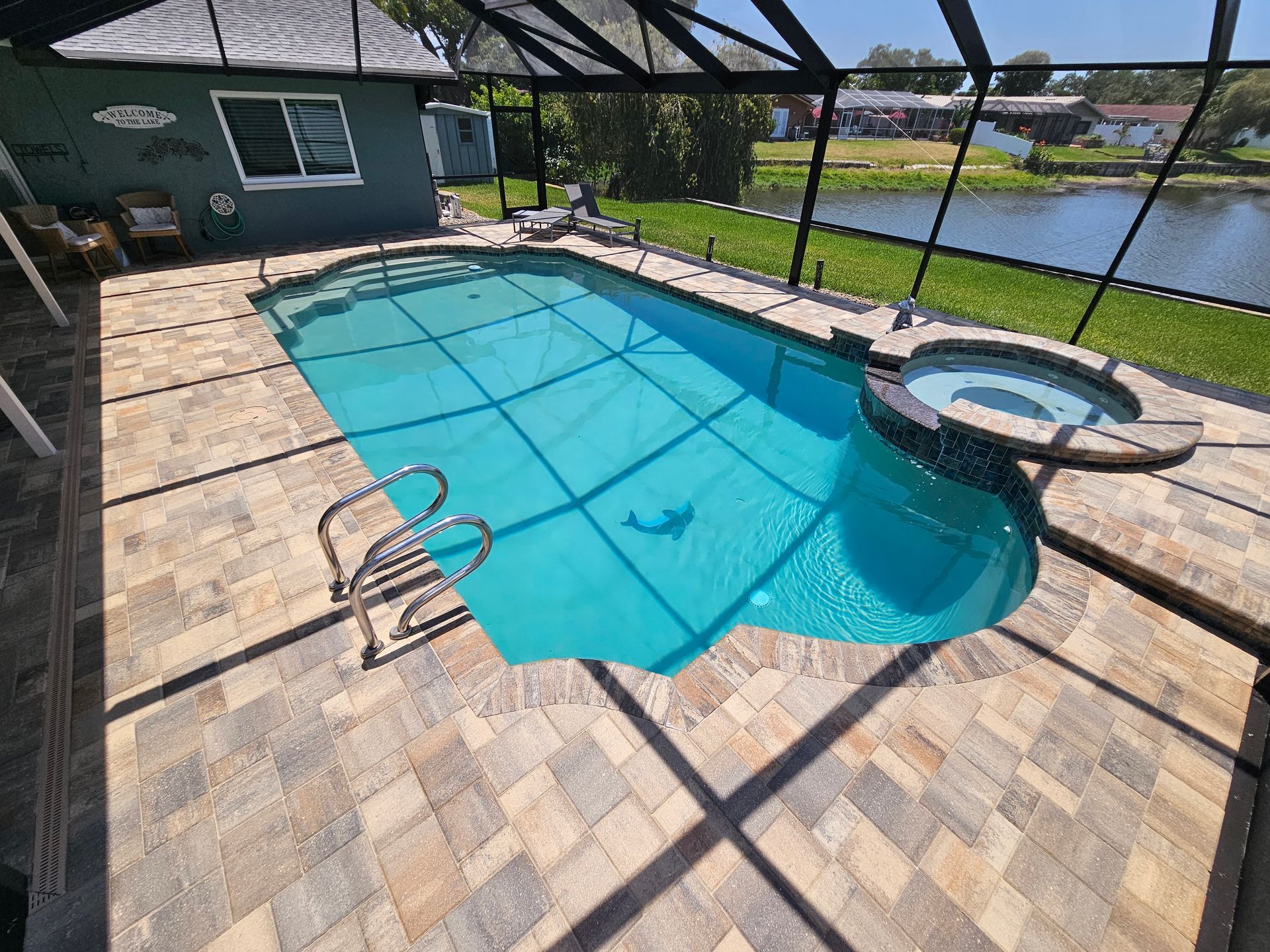 Backyard with an above-ground pool, gray paver patio, white fence, and a small building.