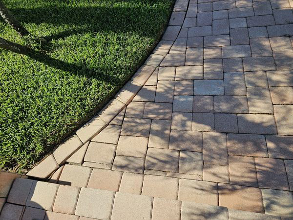 Curved brick walkway borders green grass, sunny outdoor setting.