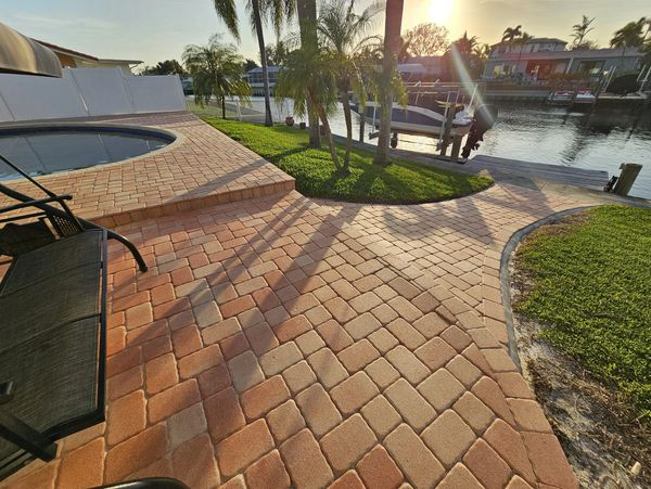 Brick patio with steps leading to a dock and waterway. Palm trees, grass, and sunlight.