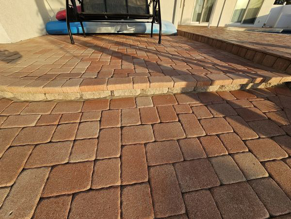 Brick patio with steps, red-brown pavers. A swing and a light blue inflatable are in the background.