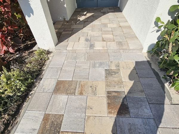 Brick walkway leading to a doorway, with colorful pavers in an outdoor setting.
