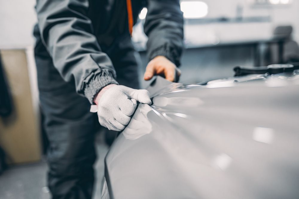 A Man Is Wrapping a Car with Plastic Film — Jetty Car Detailing Coffs Harbour in Coffs Harbour NSW