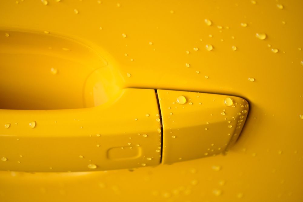 A Close up Of a Yellow Car Door Handle with Water Drops on It — Jetty Car Detailing Coffs Harbour in Coffs Harbour NSW