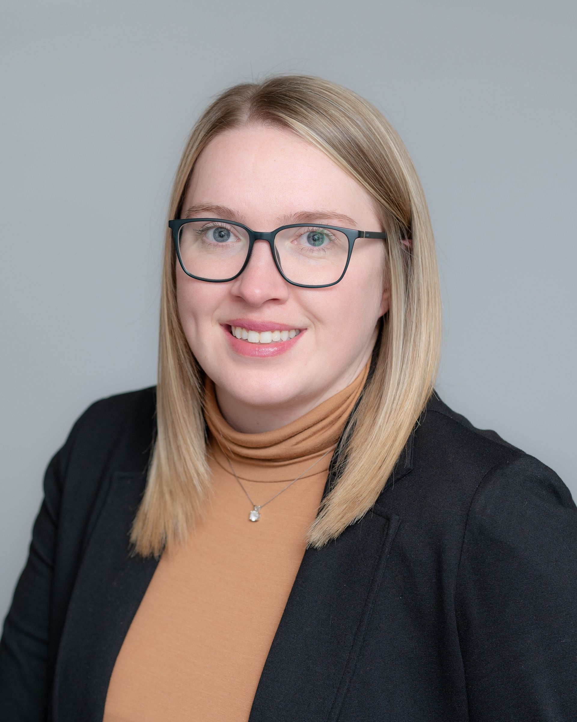 A woman wearing glasses and a black jacket is smiling for the camera.