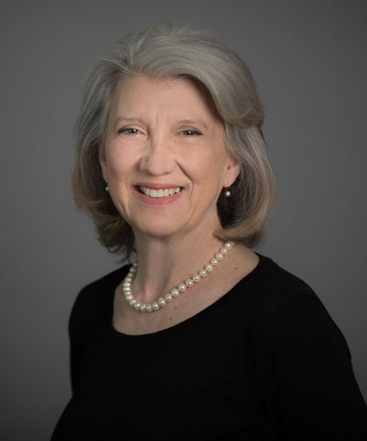 A woman wearing a black shirt and a pearl necklace is smiling.