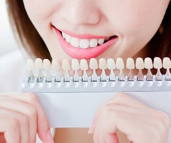 Woman smiling, holding a teeth shade guide, comparing shades to her bright white teeth.