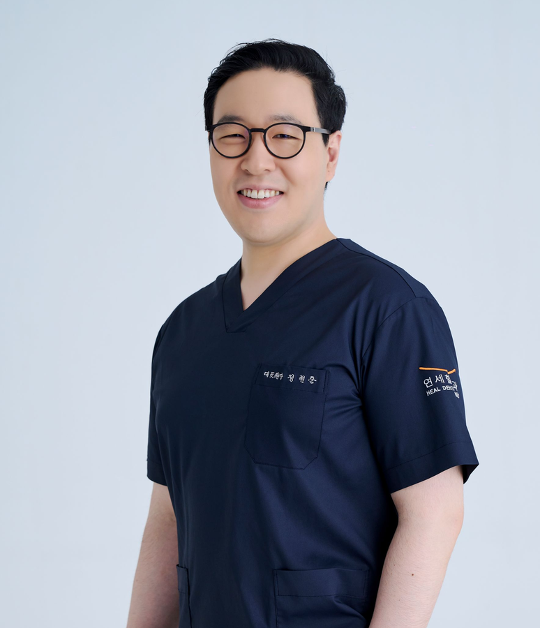 Smiling man in blue scrubs, wearing glasses, against a white background.