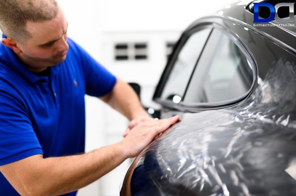 A man in a blue shirt is covering a car with plastic wrap.