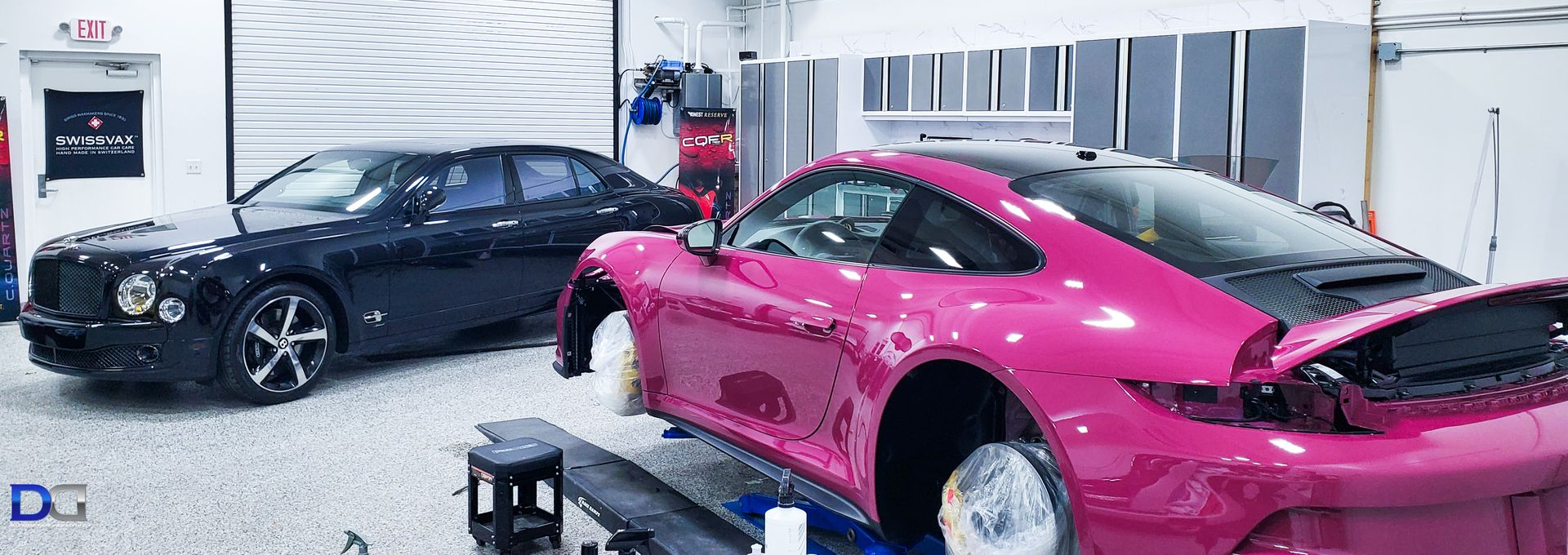 Person in black glove applying coating on a shiny, black car in a garage.