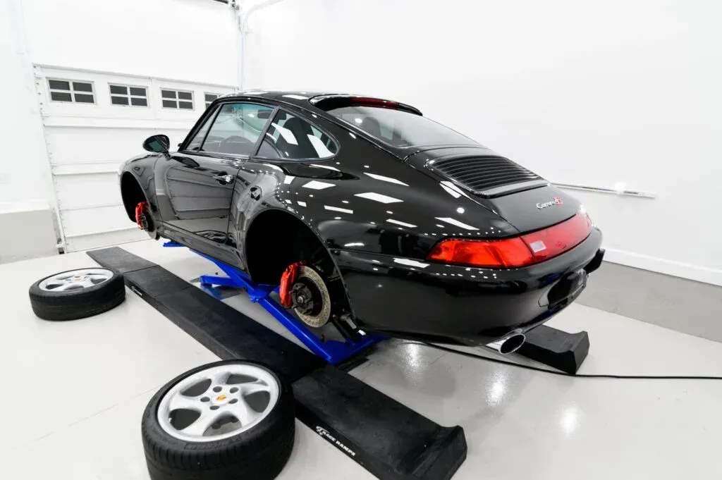 A black porsche is sitting on a lift in a garage.