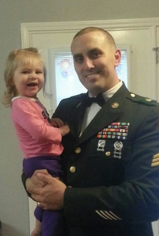 A man in a military uniform holds a little girl in his arms