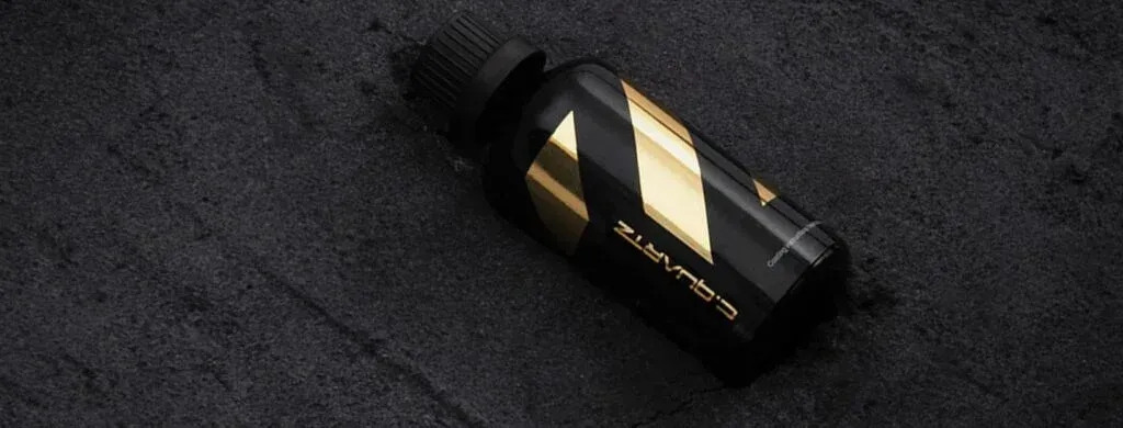 A black and gold bottle is sitting on a black surface.