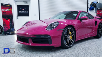 Pink Porsche 911 Turbo S parked in a garage. It has black wheels and yellow brake calipers.