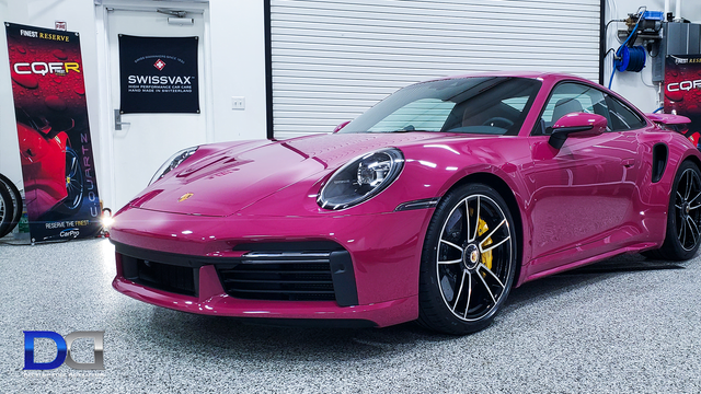 Pink Porsche 911 Turbo S parked in a garage. It has black wheels and yellow brake calipers.