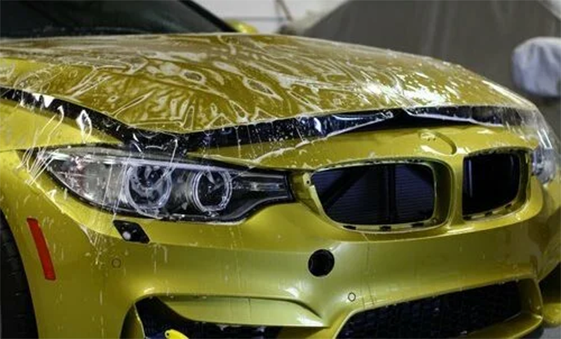 Yellow car hood with clear protective film being applied.