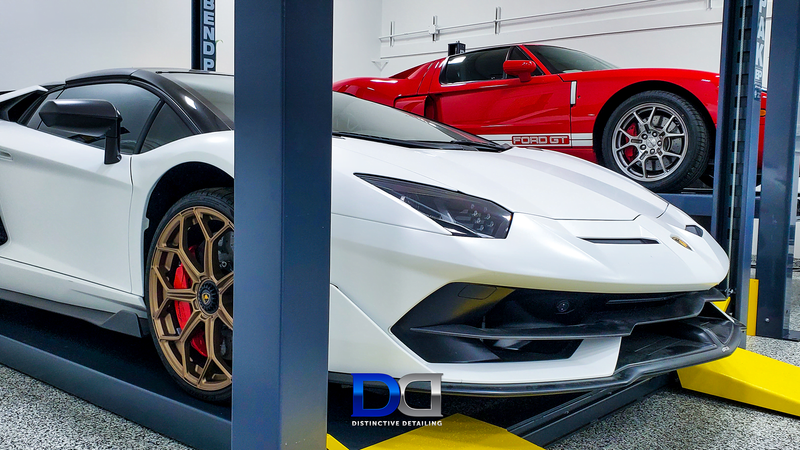 White Lamborghini and red Ford GT parked on a lift in a garage.