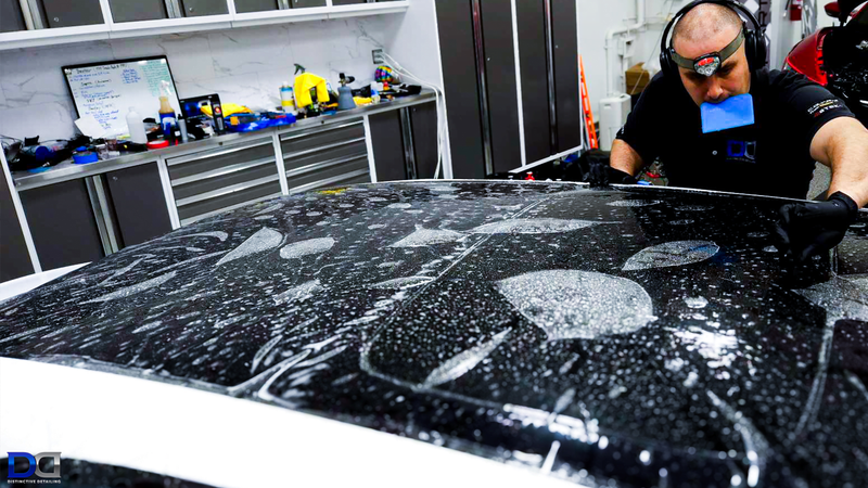 A worker applying film to a car roof in a shop. He is wearing headphones and a face mask.