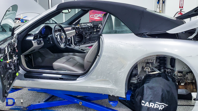 Silver convertible car on a lift with doors open, undergoing repair.