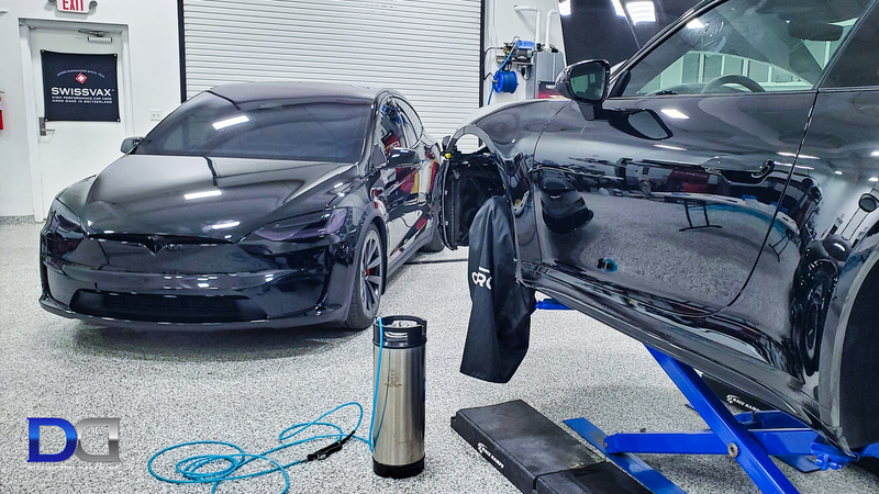 Two black cars side-by-side in a garage. One is on a lift. A water bottle and tools are on the floor.