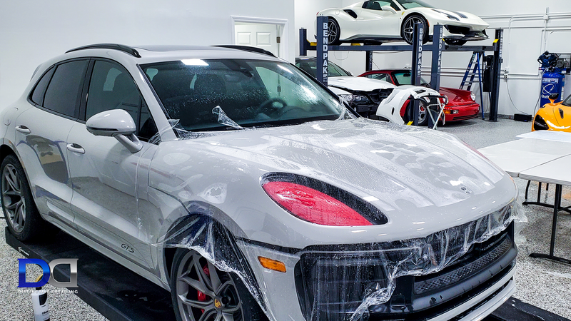White Porsche Macan with protective film in a garage with other luxury cars.
