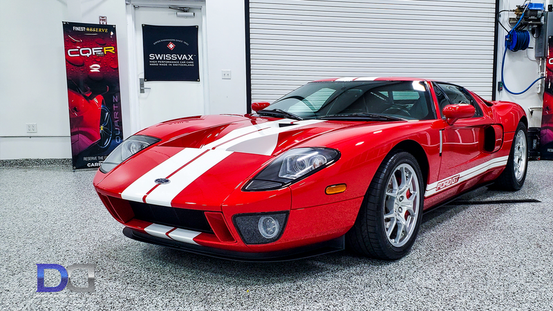 Red Ford GT sports car with white stripes parked in a garage.