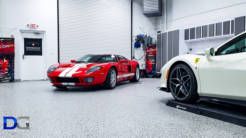 Red Ford GT and white Ferrari in a modern garage with grey flooring and cabinets.