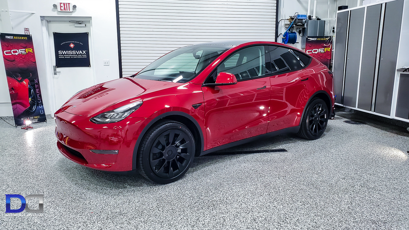 Red Tesla Y with black wheels parked inside a brightly lit shop.