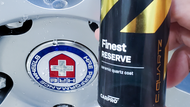 A hand holding a CARPRO Finest Reserve ceramic quartz coat bottle over a wheel with the HRE Performance Wheels logo.
